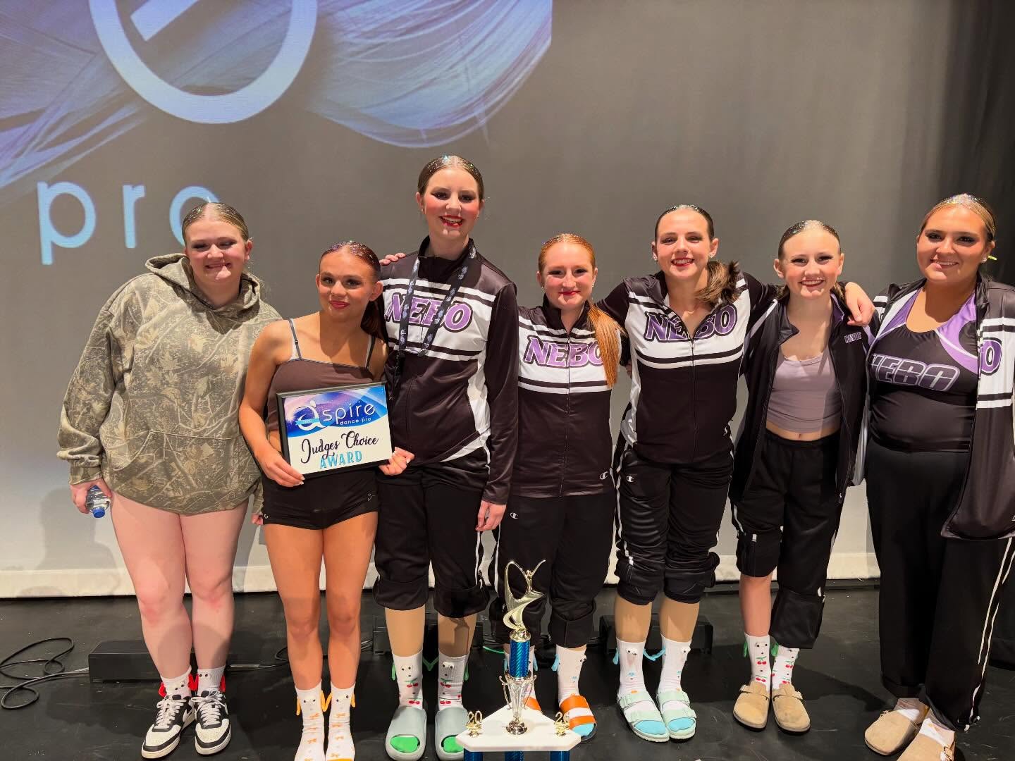 Dancers holding a Judges Choice award and a tall trophy on stage